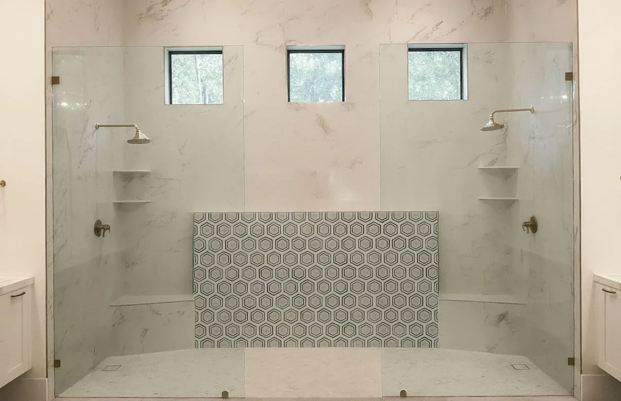Glass-enclosed double shower with marble-look tile, a hexagon tile accent, and a built-in bench by M&H Construction & Design